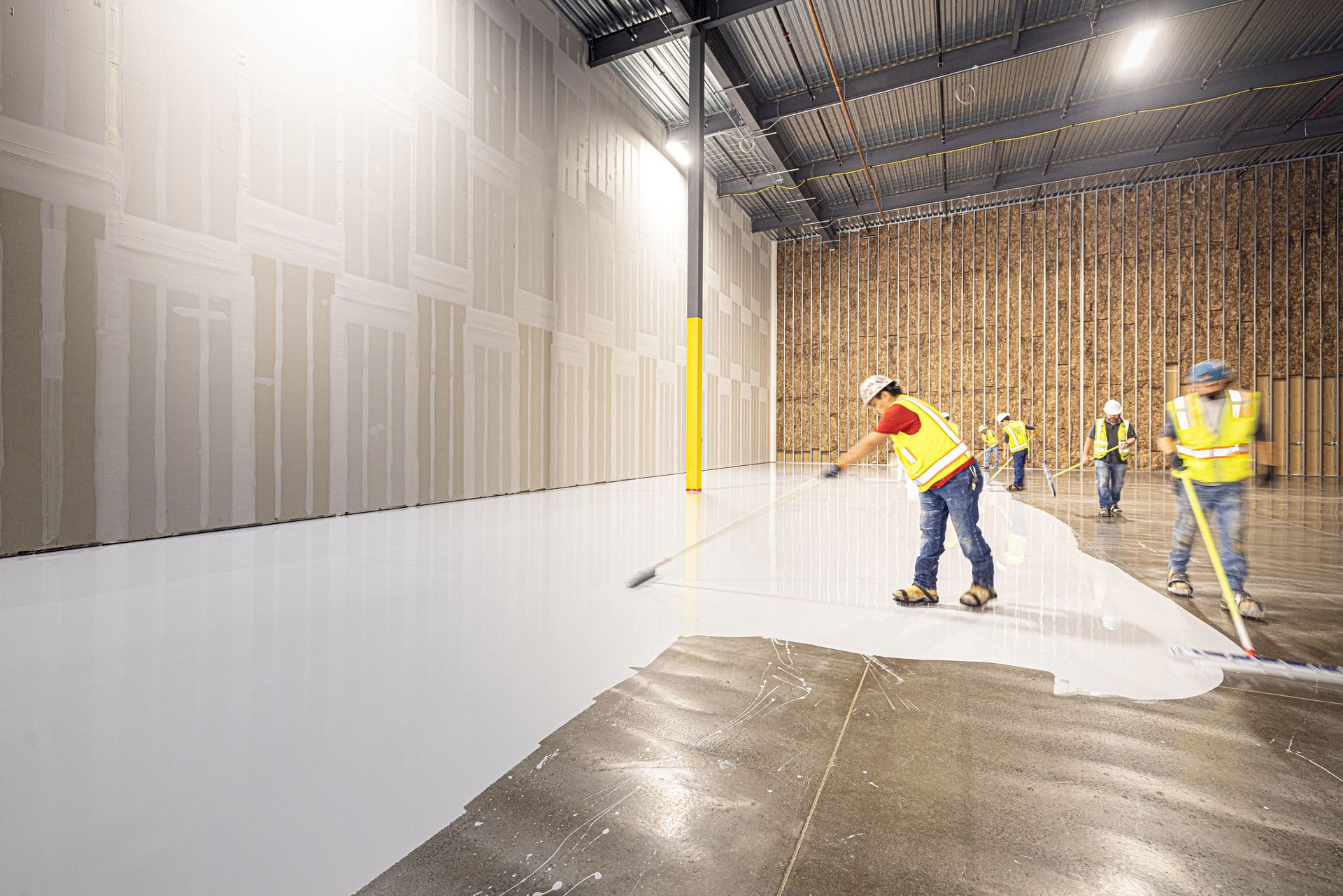 Construction workers in hard hats and vests laying a fresh concrete floor inside a building in Dallas, Texas.